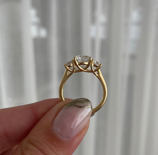 Gold ring with a diamond held by a hand against a neutral background