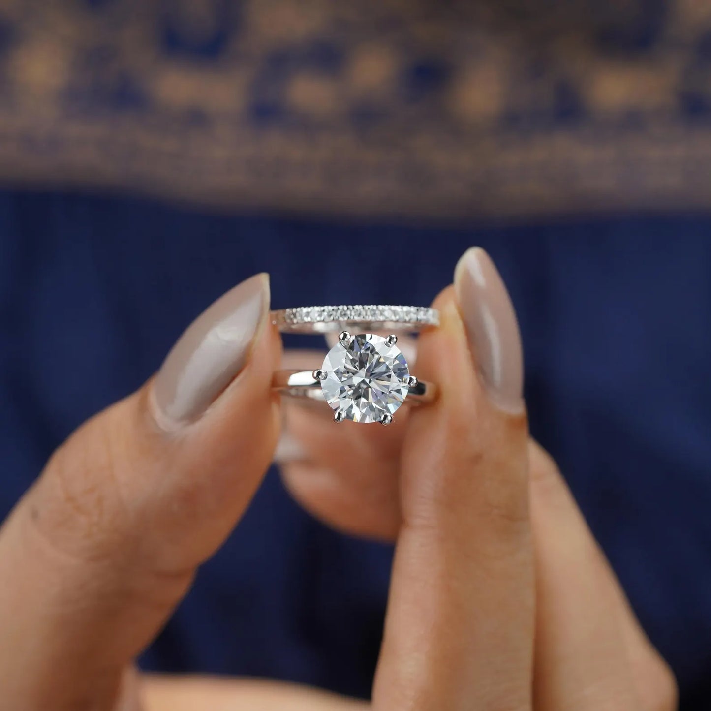 Diamond ring held between fingers against a blurred background