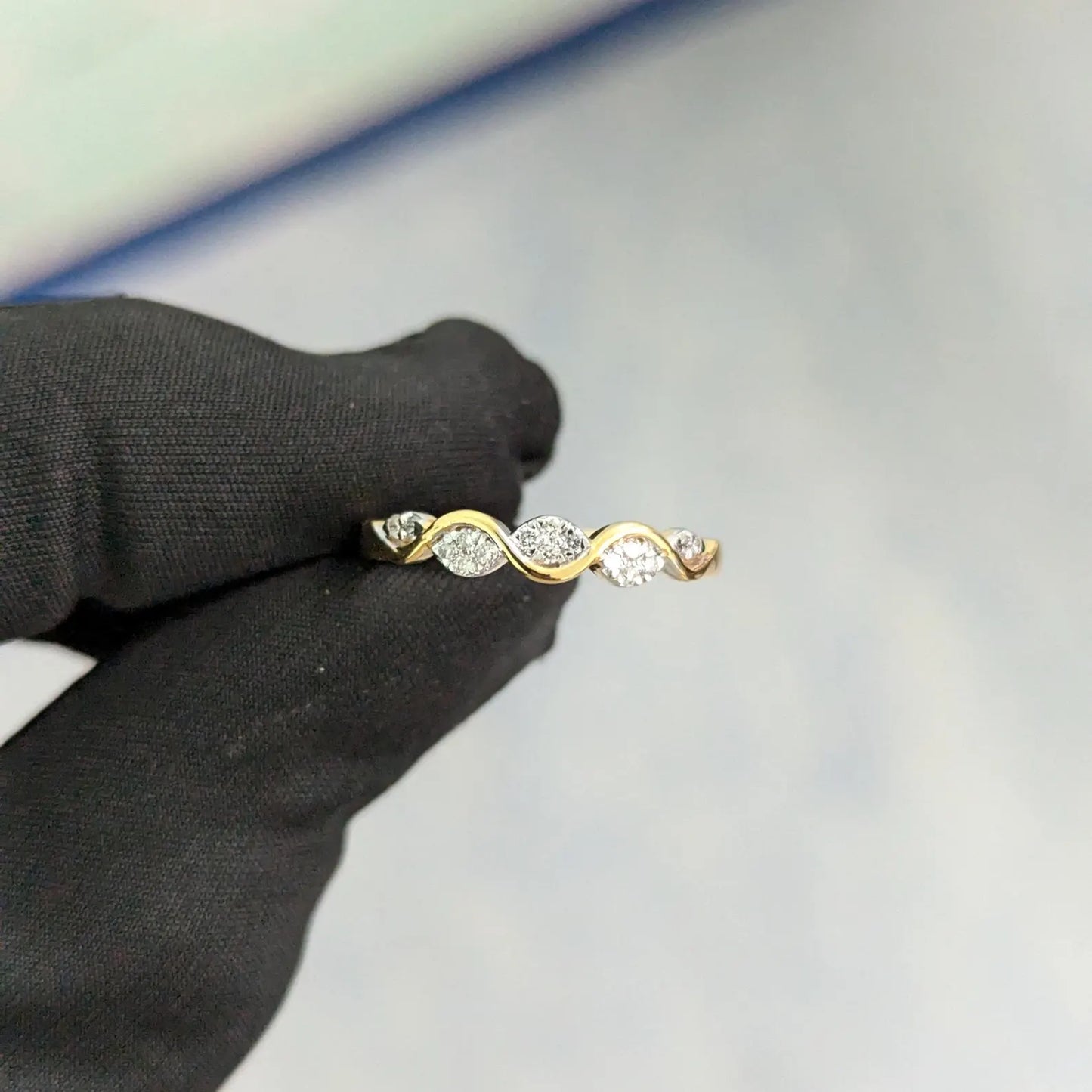 Gold ring with three diamonds held by a black-gloved hand on a light gray background