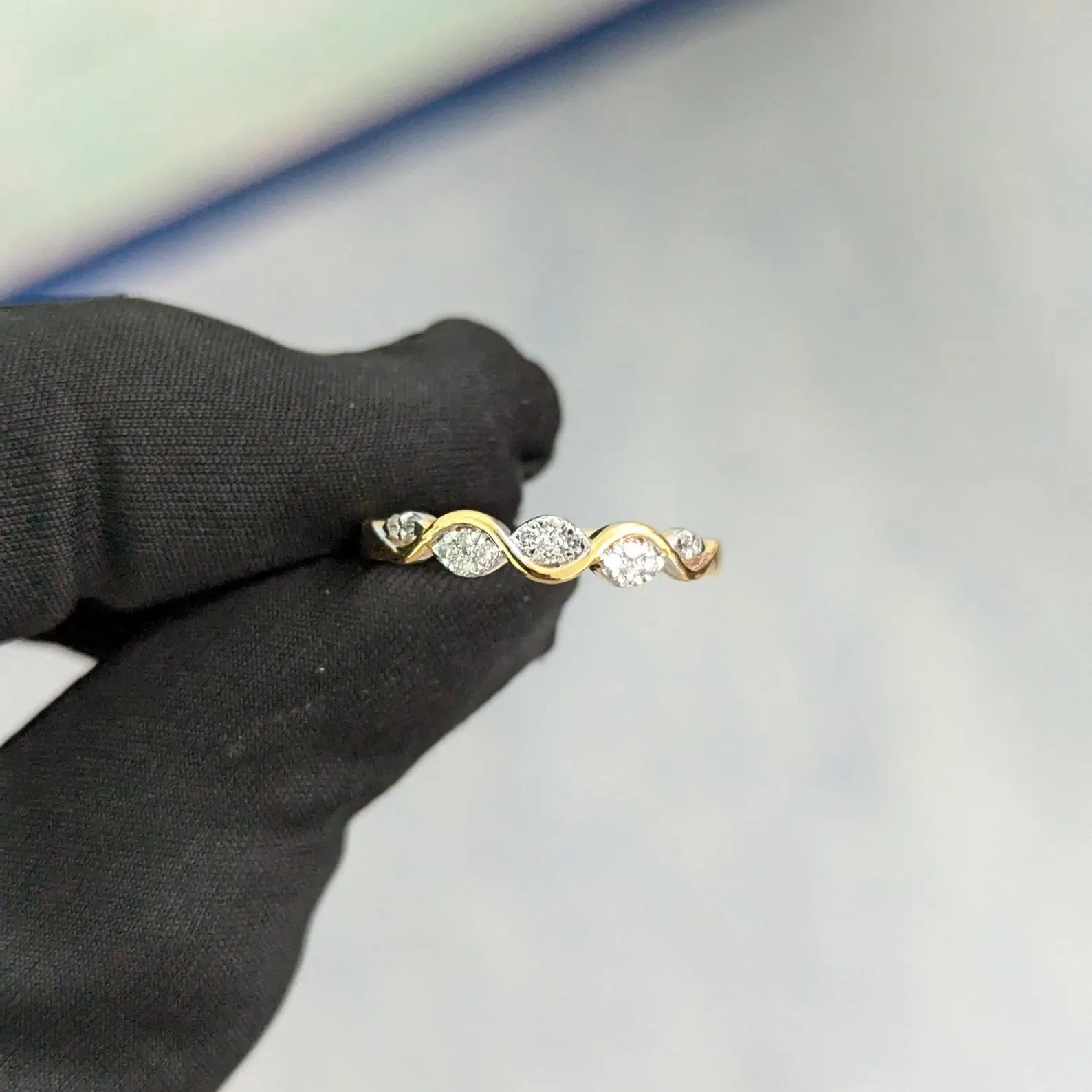 Gold ring with three diamonds held by a black-gloved hand on a light gray background